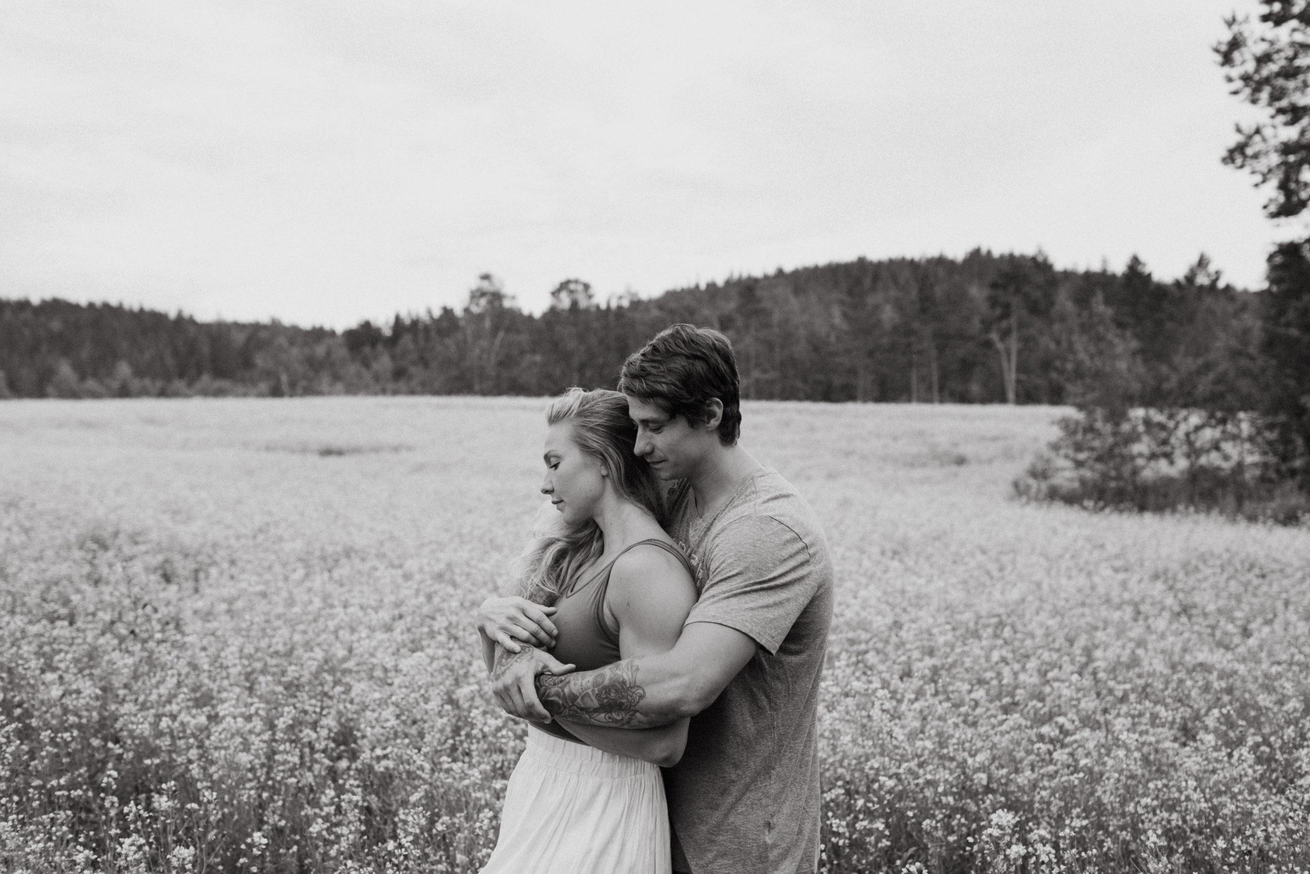 Man hugging his fiancé behind her back at a field of rapeseeds in Finland